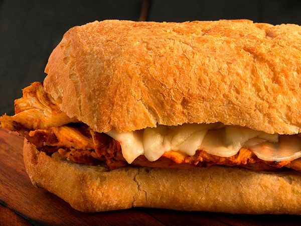 Un primer plano de un sándwich de pollo en un pan sobre una mesa de madera.