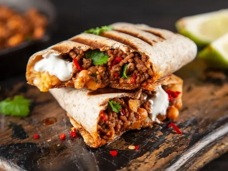 Un burrito se corta por la mitad en una tabla de cortar de madera.