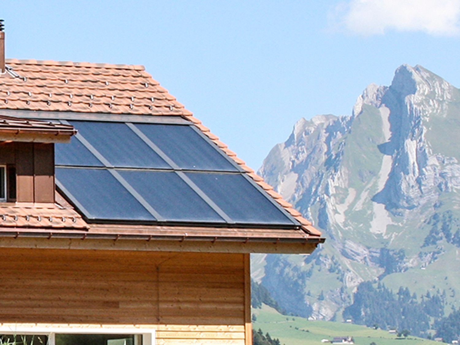 Ein Haus mit Sonnenkollektoren auf dem Dach und Bergen im Hintergrund