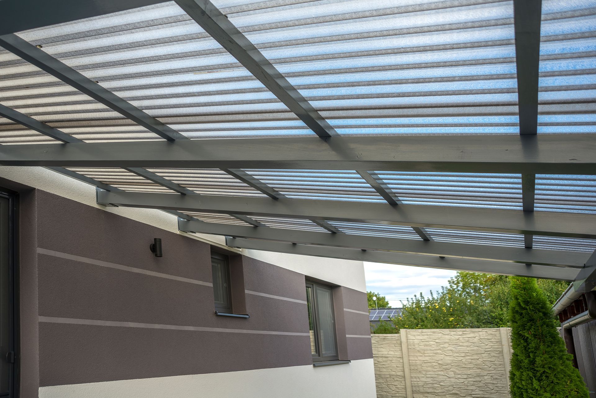 A carport with a clear roof is attached to the side of a house.