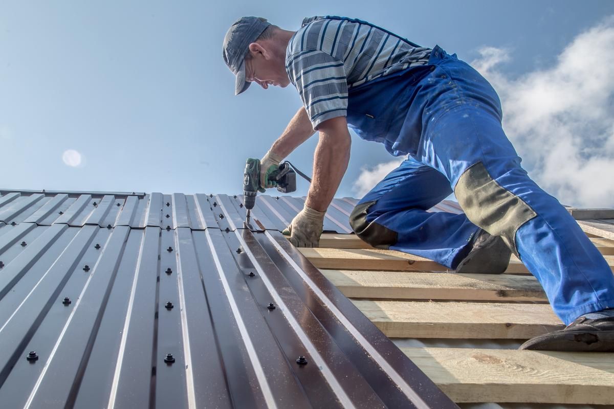 Image of a roofer in blue overalls fixing a metal roof.