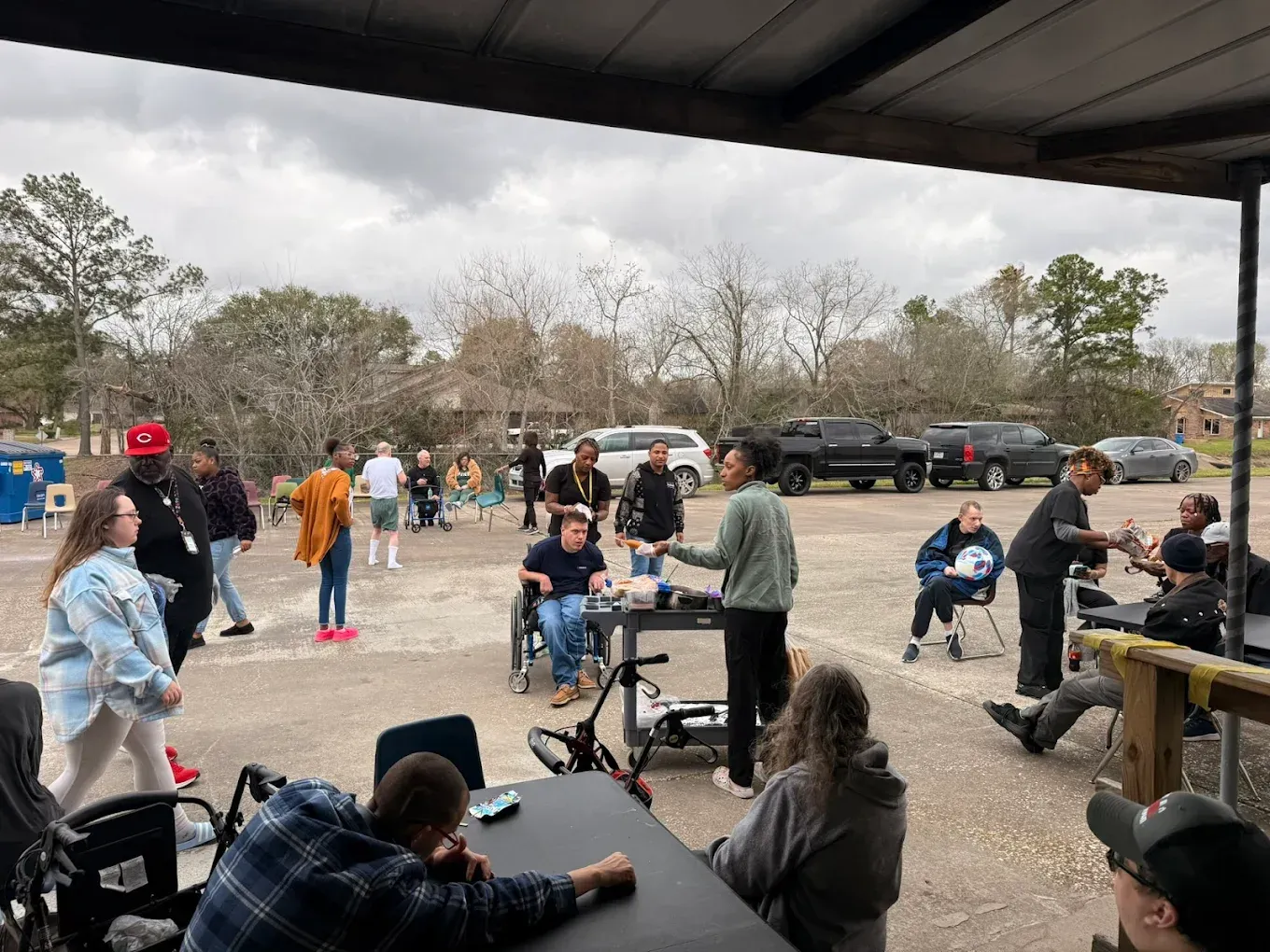 A group of people are sitting at tables in a parking lot.