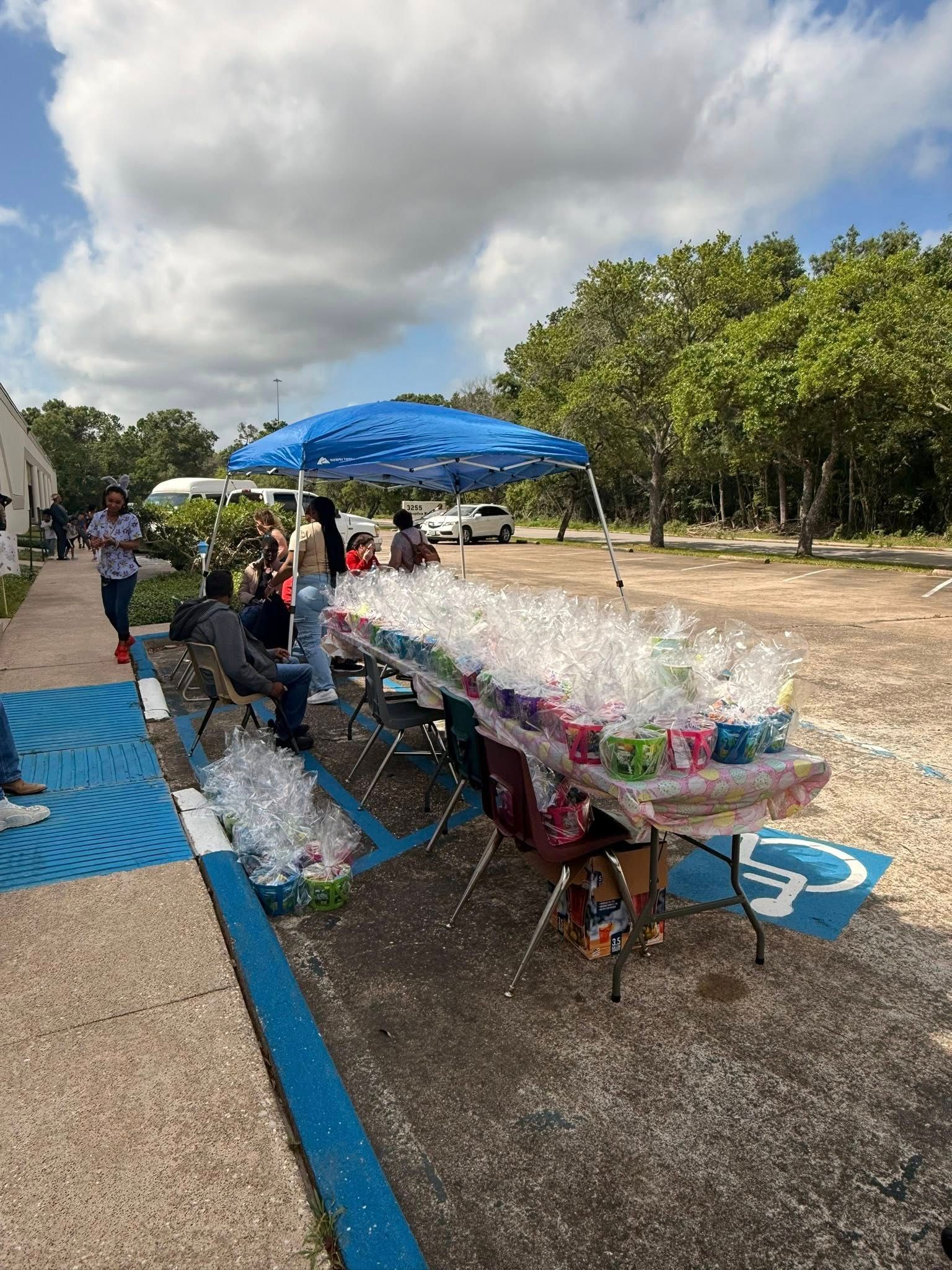 A group of people are sitting at tables in a parking lot.