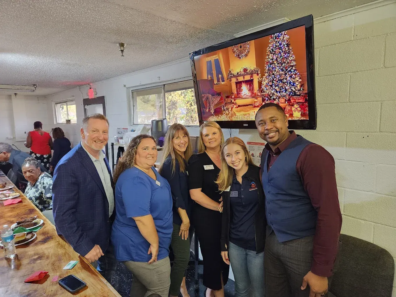 A group of people are posing for a picture in front of a television with a christmas tree on it.
