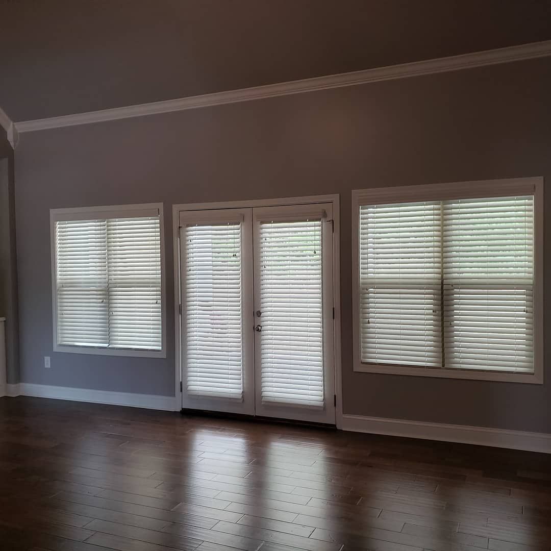 A room with dark wood floors, gray walls, and white trim. Three windows with blinds.