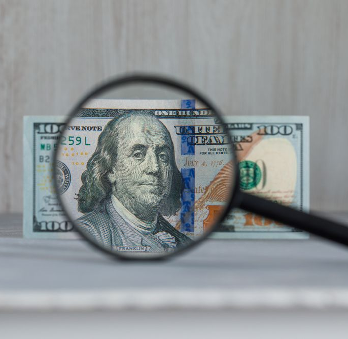 A $100 bill viewed through a magnifying glass, showing Benjamin Franklin's face.