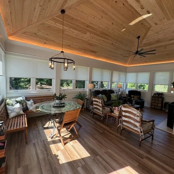 Sunroom with wood ceiling and floor, furnished with seating, round table, and plants.