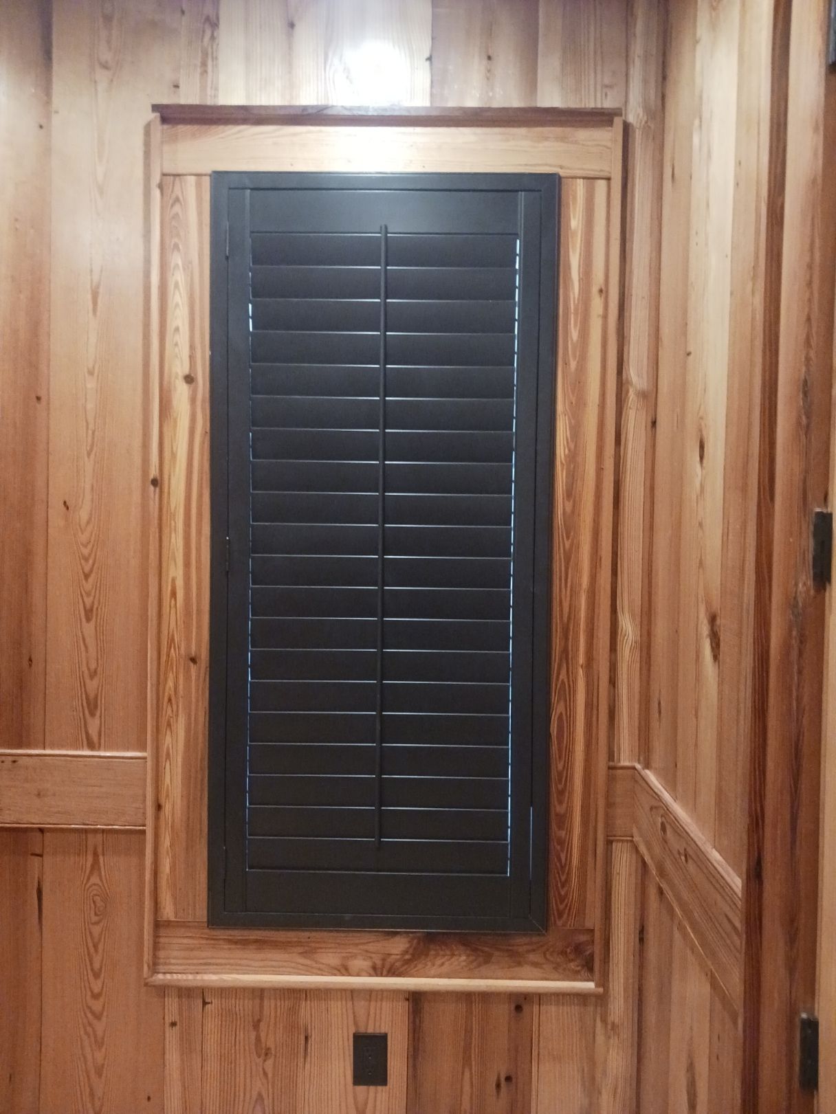 A window with black shutters on a wooden wall.