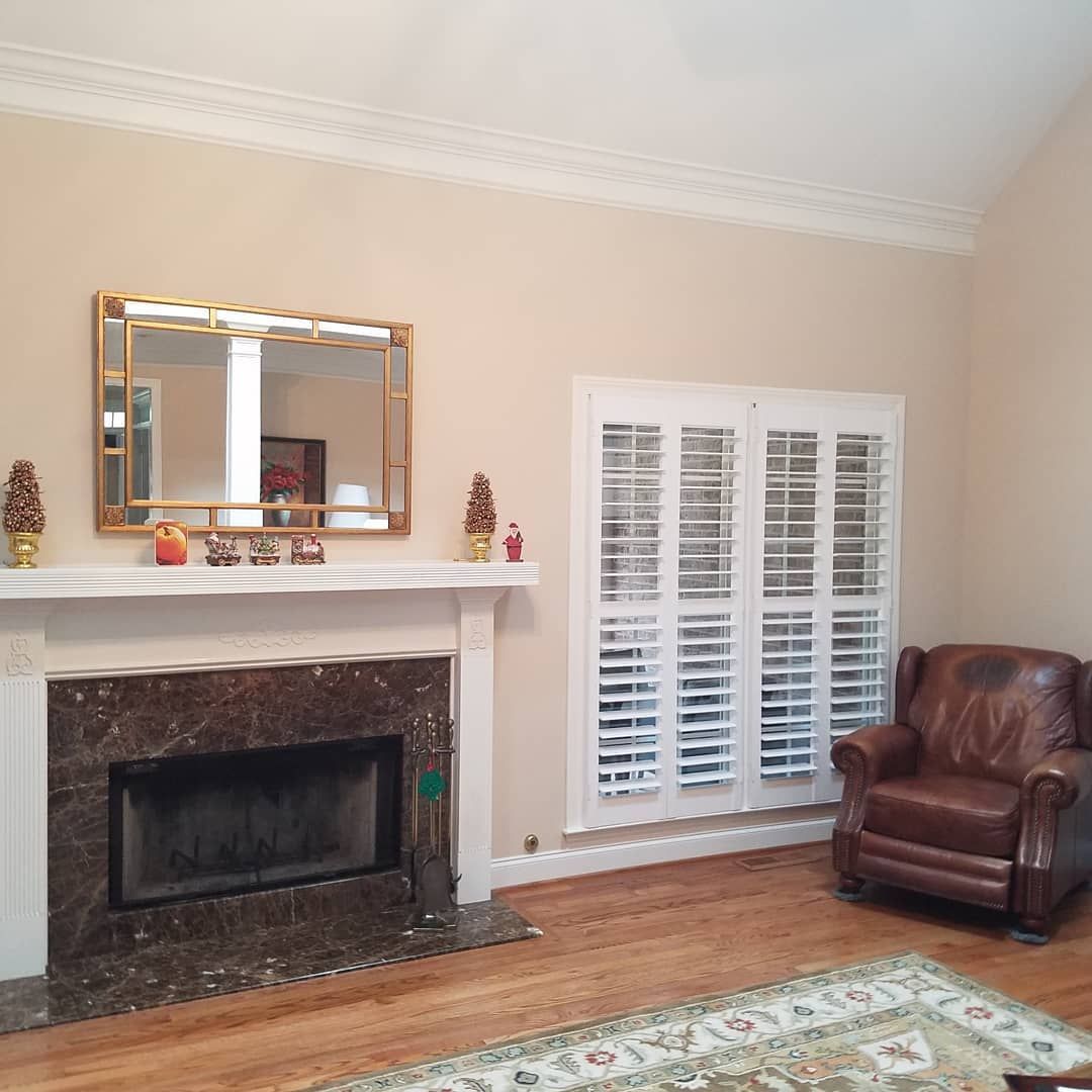 Fireplace with marble surround, gold-framed mirror, white shutters, brown leather armchair, and beige walls.