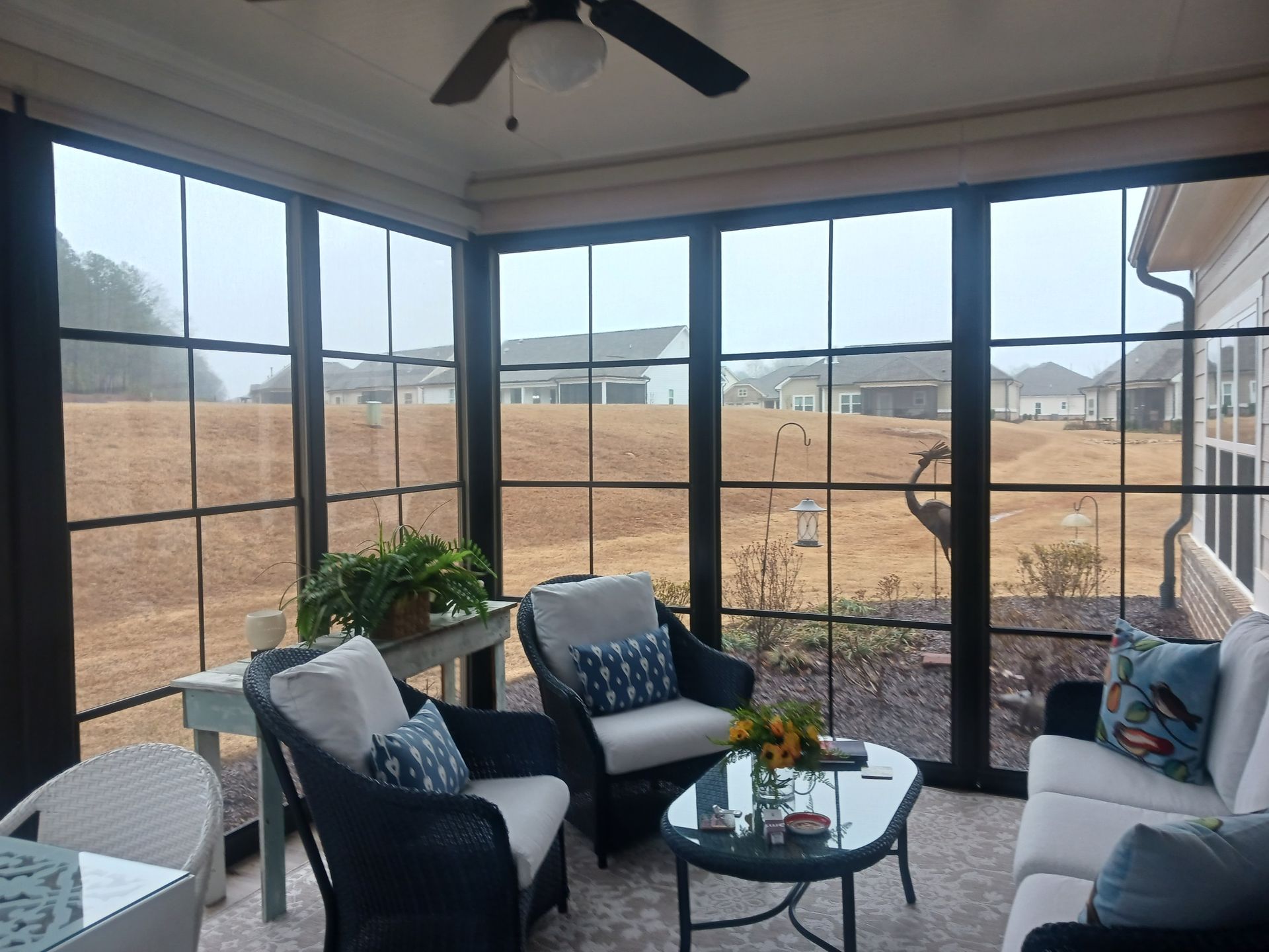 A screened in porch with a couch , chairs , table and ceiling fan.