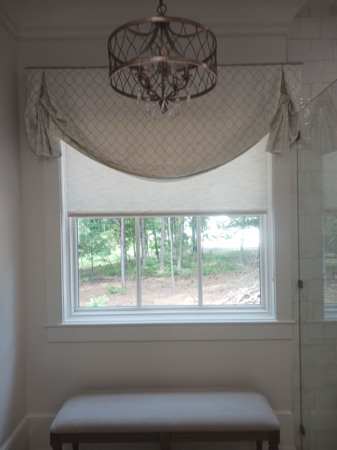 There is a bench in front of a window with a chandelier hanging from the ceiling.