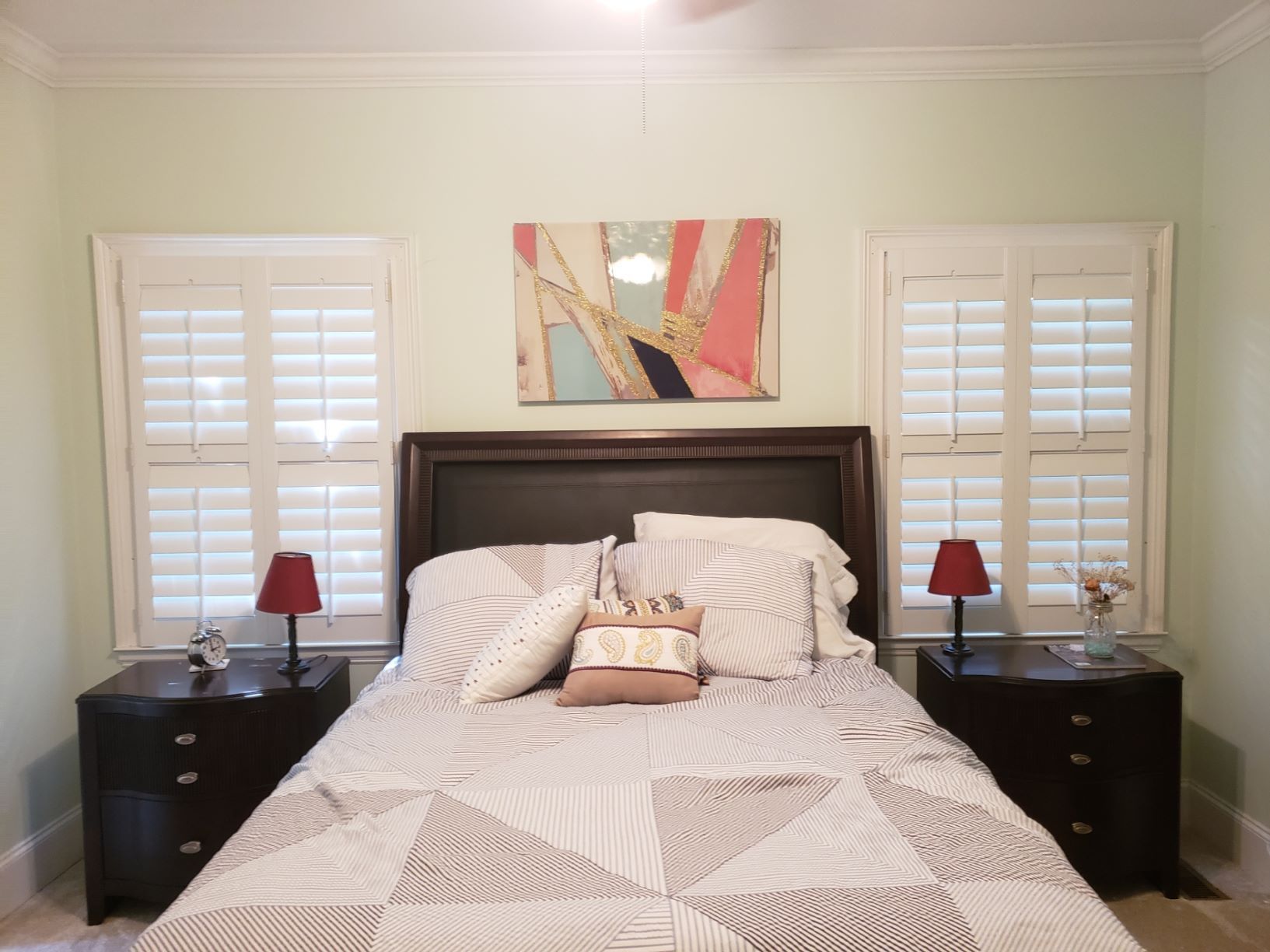 A bedroom with a bed and two nightstands and a painting on the wall above the bed