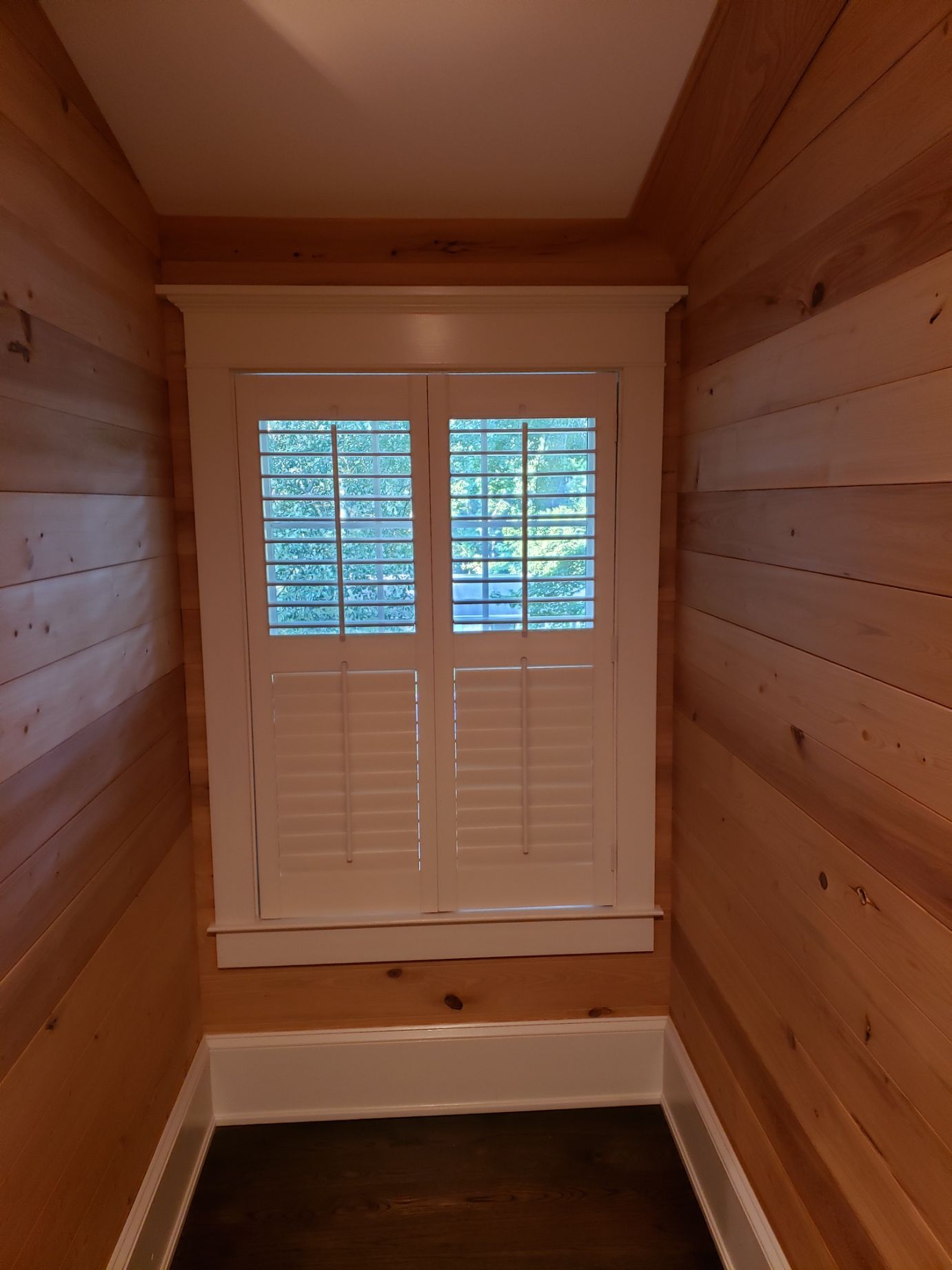 A hallway with wood paneling and a window with shutters