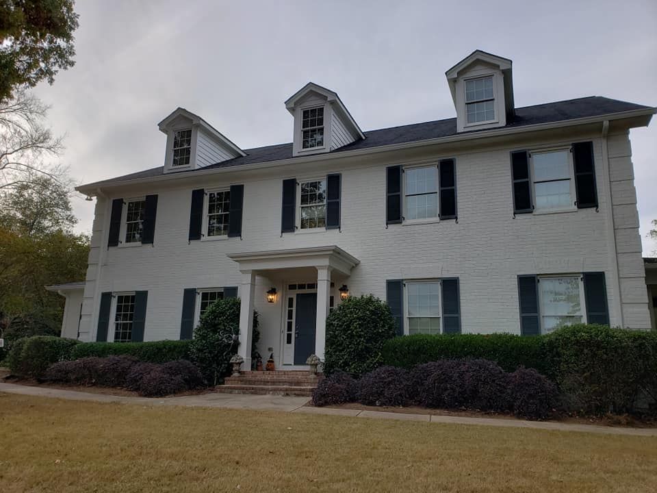 White two-story house with dark shutters and roof; three dormers on the roof.