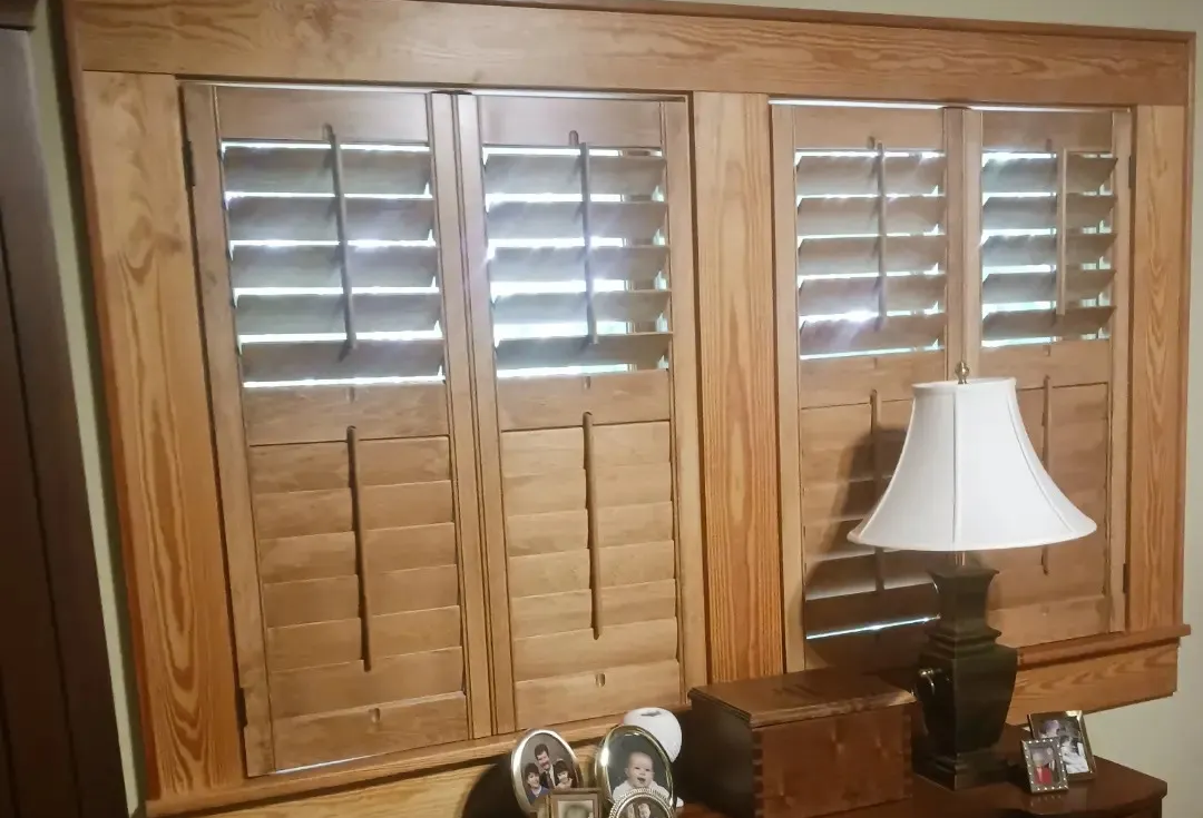 Wooden shutters and desk beneath a window. Lamp, photos, and decor on the desk.