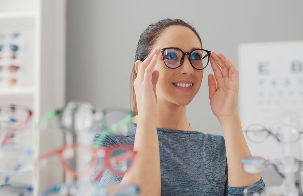 Woman Smiling While Trying on Glasses in an Optician’s Shop — Peninsula Eyecare Izzards Optometrists in Woy Woy, NSW