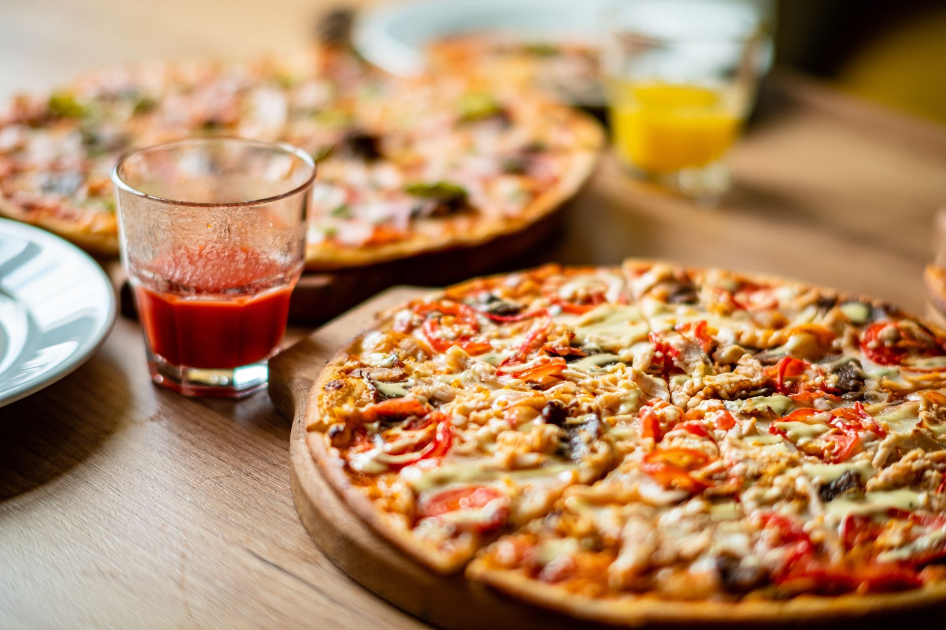 Pizzas on wooden board with a glass of red liquid, and orange juice, on a table.