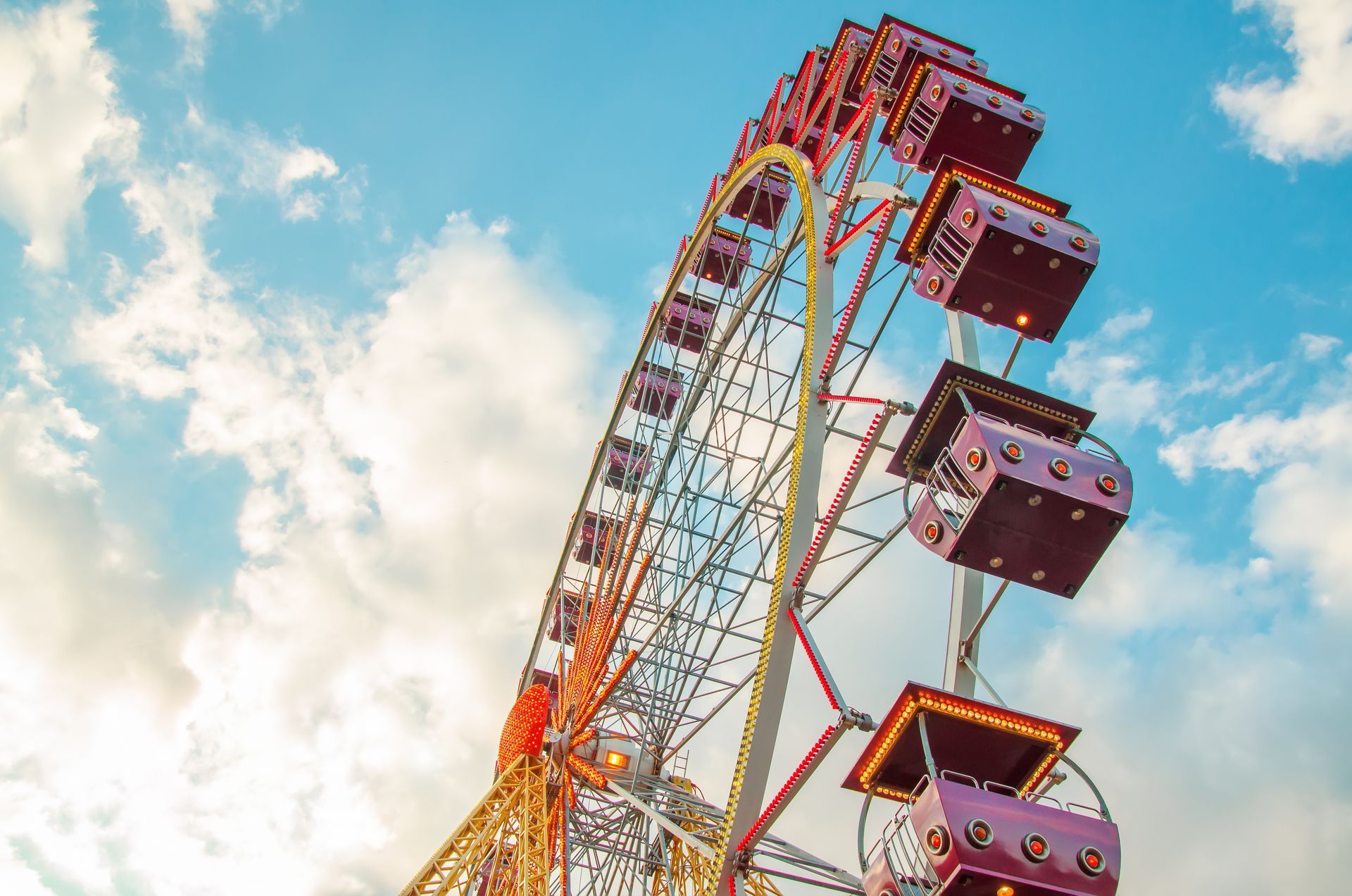 Ferris wheel against a partly cloudy blue sky; illuminated booths.
