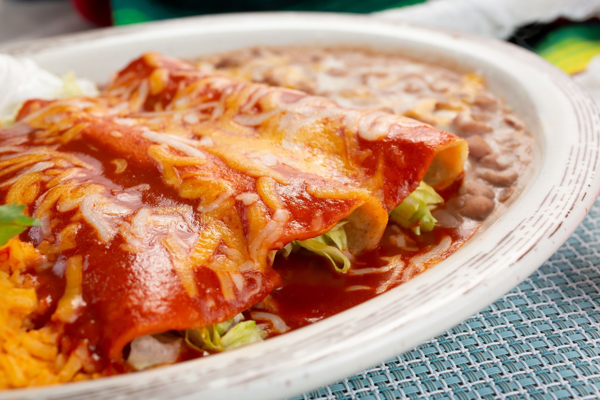 Enchiladas covered in red sauce and cheese, with refried beans and rice on a plate.
