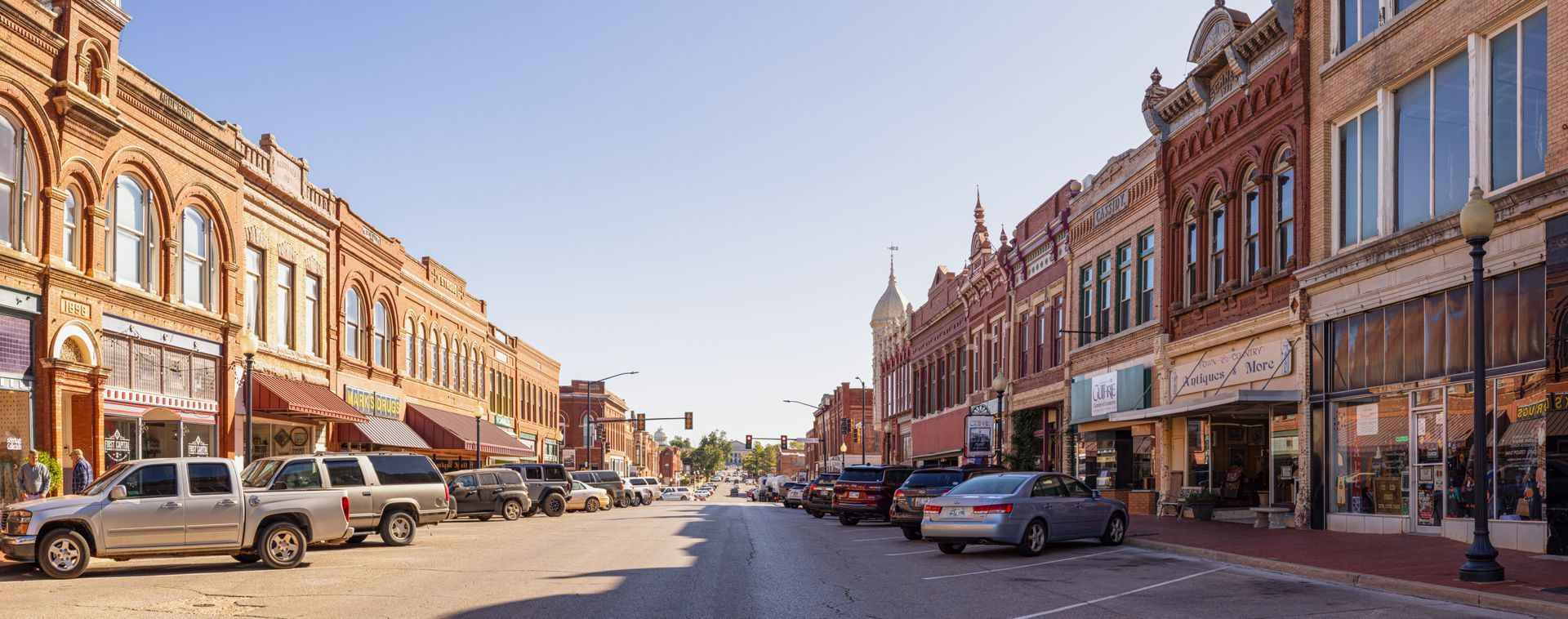 Street lined with brick buildings and parked cars, under a clear blue sky.