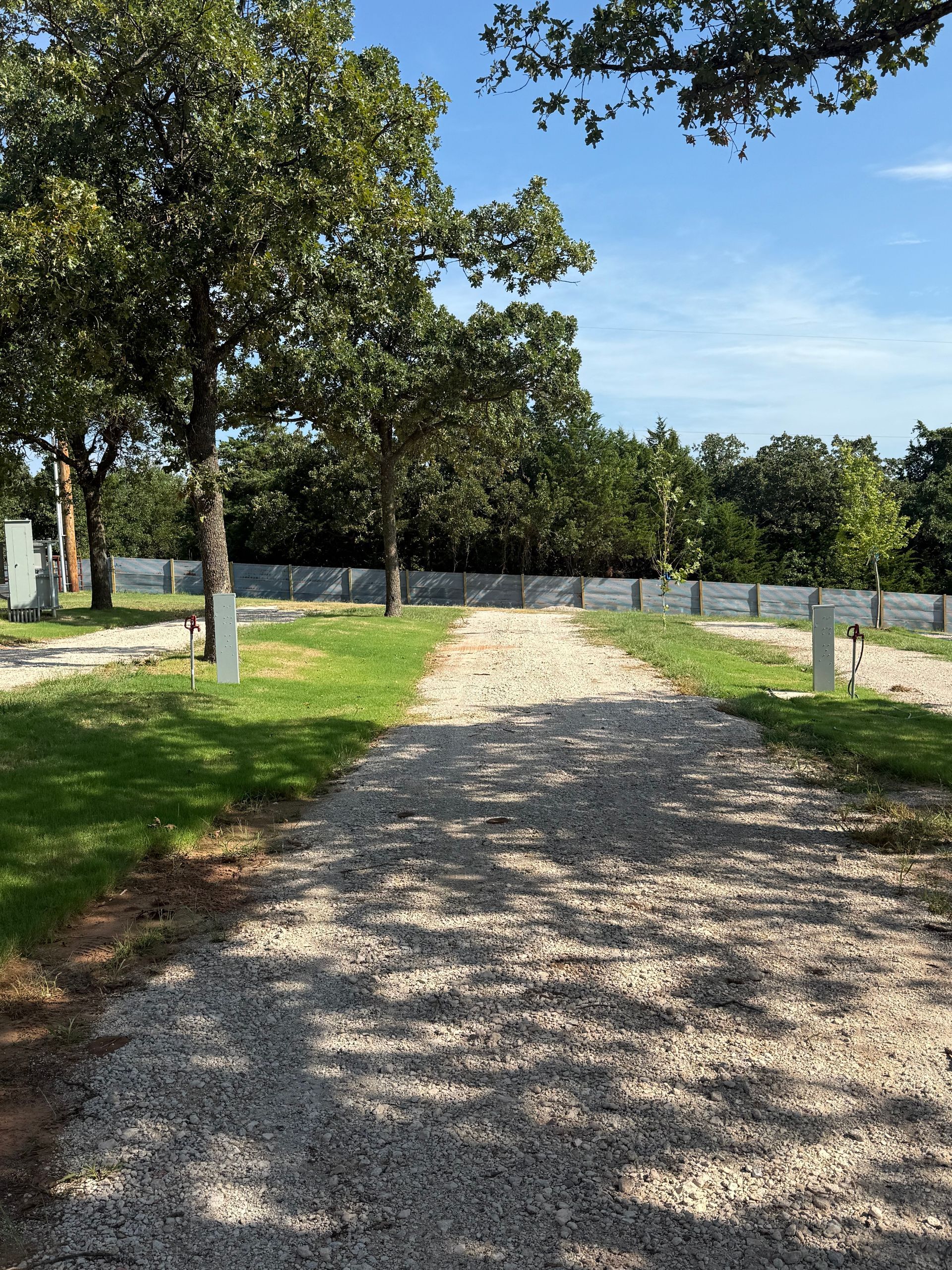 Gravel path through a cemetery with headstones on both sides, trees, and a blue sky.