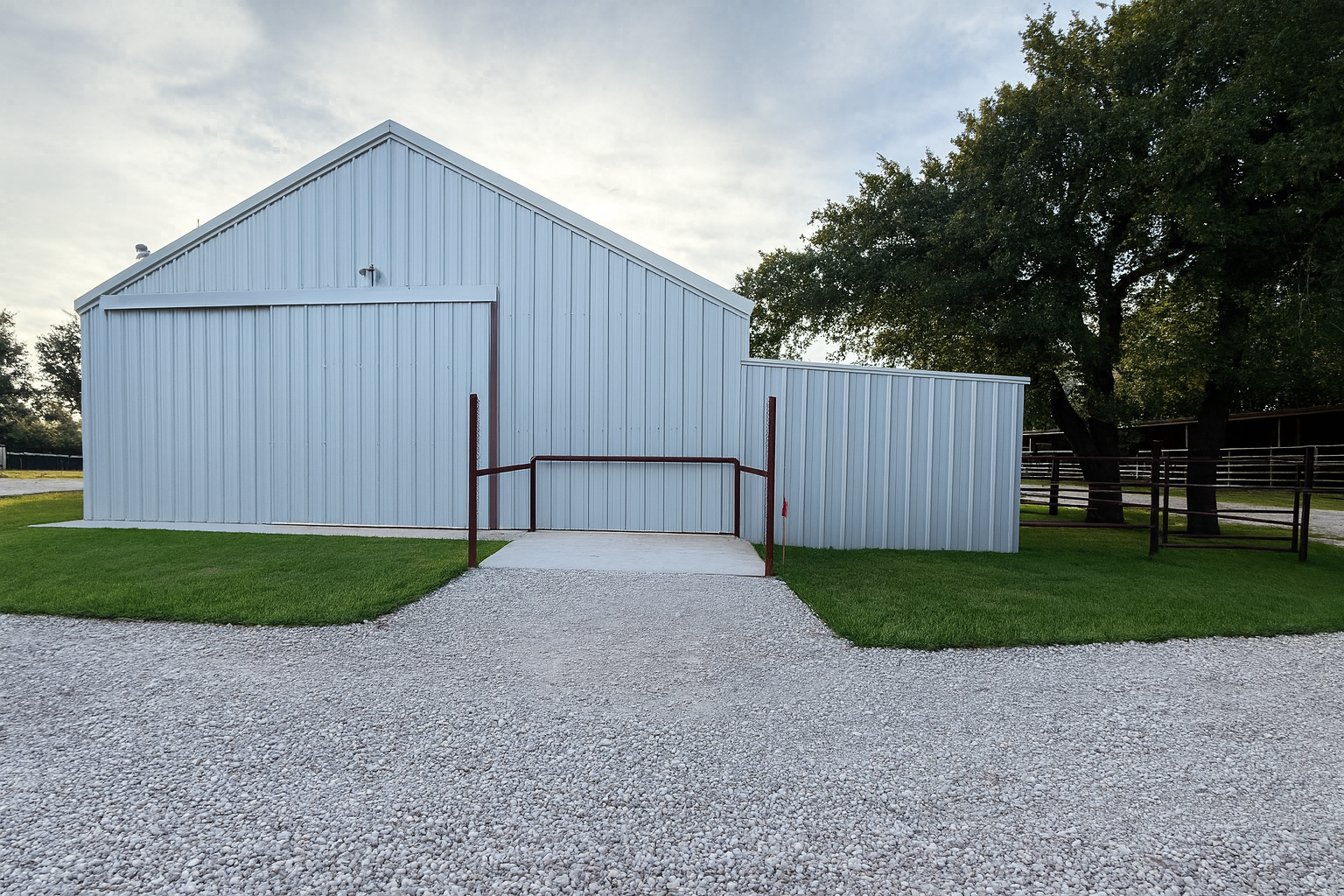 White metal barn with gravel path and green grass under overcast sky.