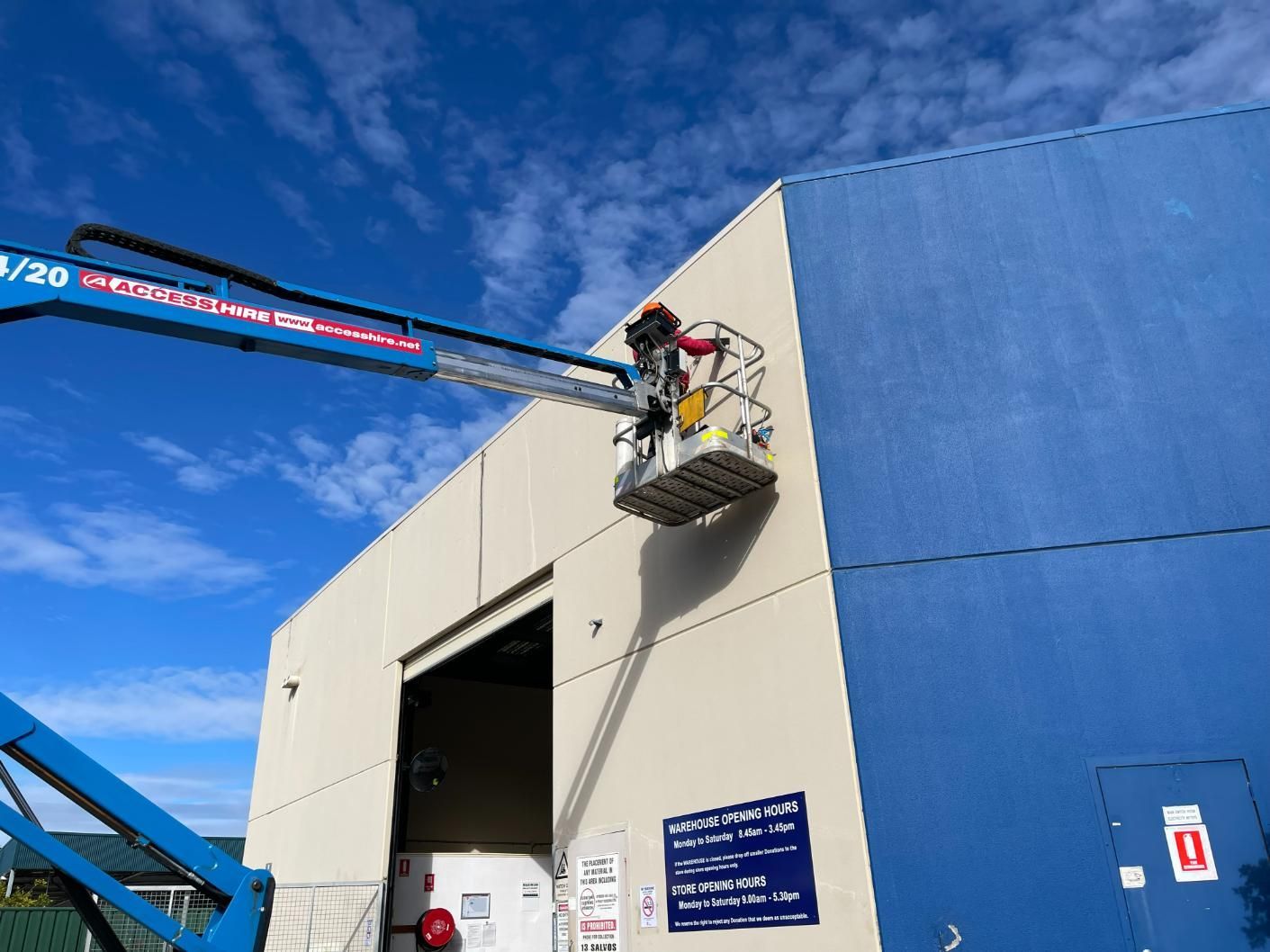 A Man is Working on a Light on the Side of a Building — Gunter Electrical In Kariong, NSW