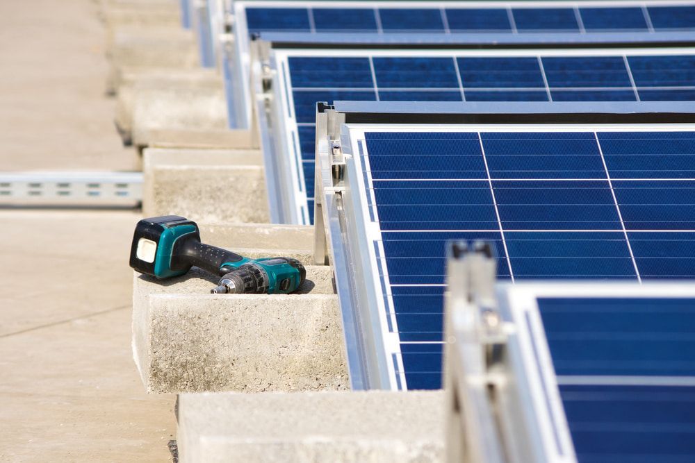 A Drill is Sitting on a Concrete Block Next to a Row of Solar Panels — Gunter Electrical In Kariong, NSW
