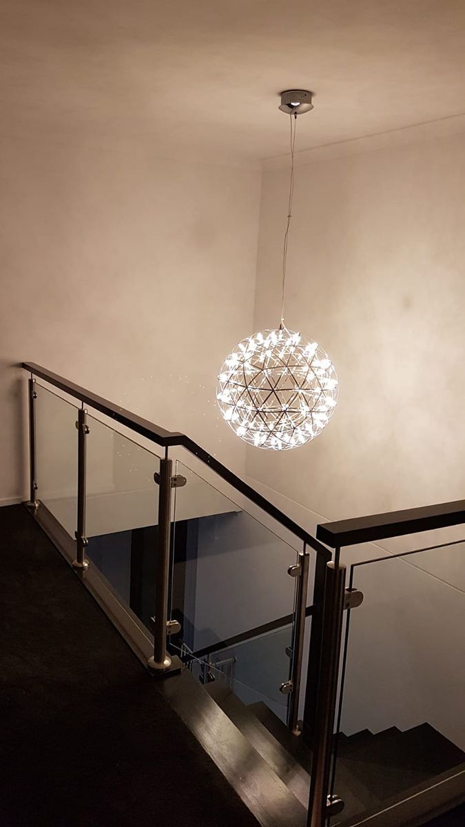 A Staircase With a Glass Railing and a Chandelier Hanging From the Ceiling.