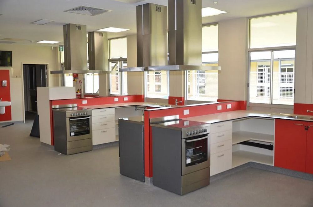 A Kitchen With Red Cabinets and Stainless Steel Appliances — Designer Kitchens in Berrimah, NT