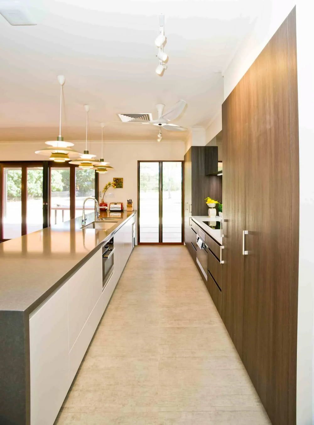 A Long Kitchen With a Lot of Cabinets and a Ceiling Fan — Designer Kitchens in Berrimah, NT
