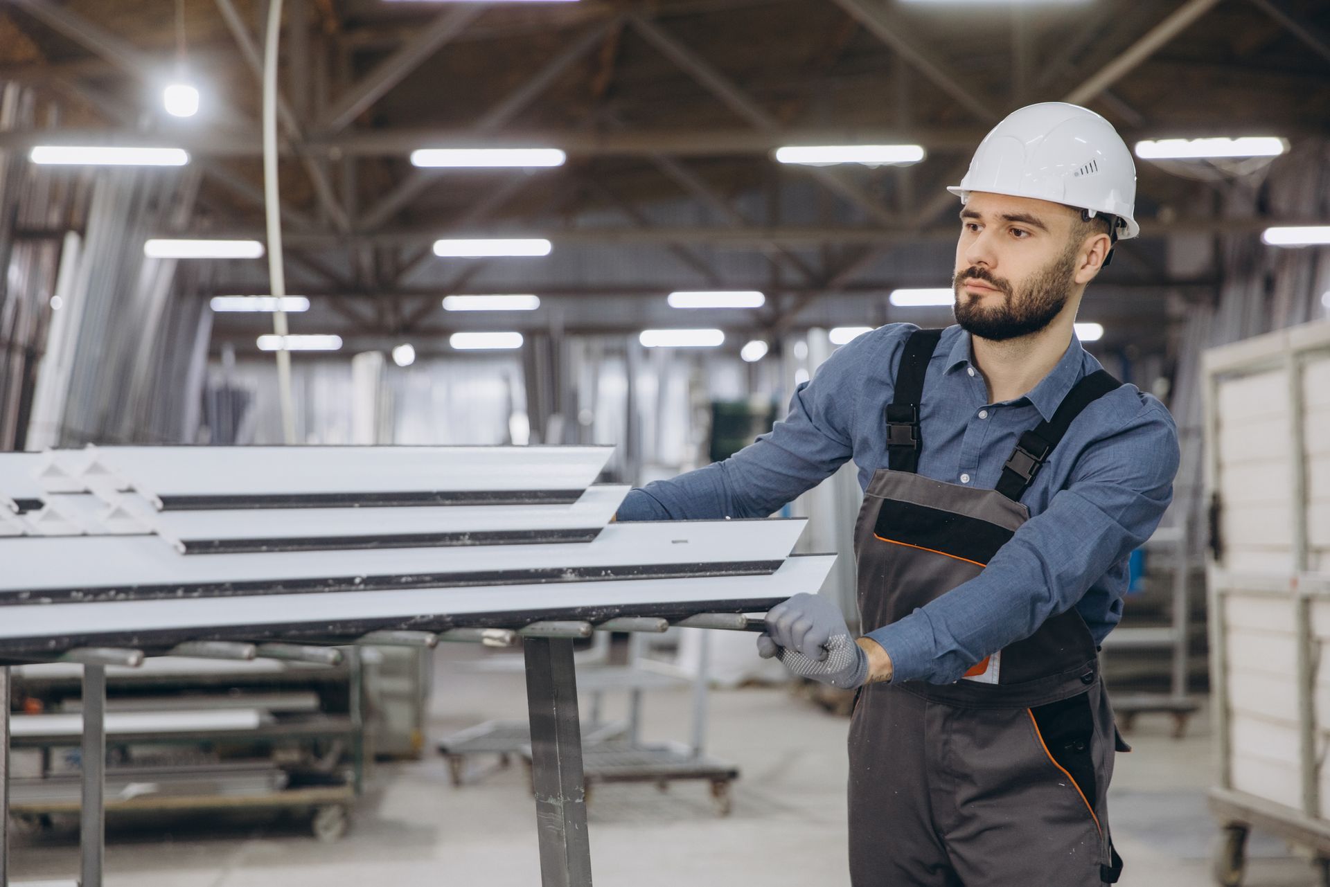 Factory worker moving aluminum window profiles in warehouse 