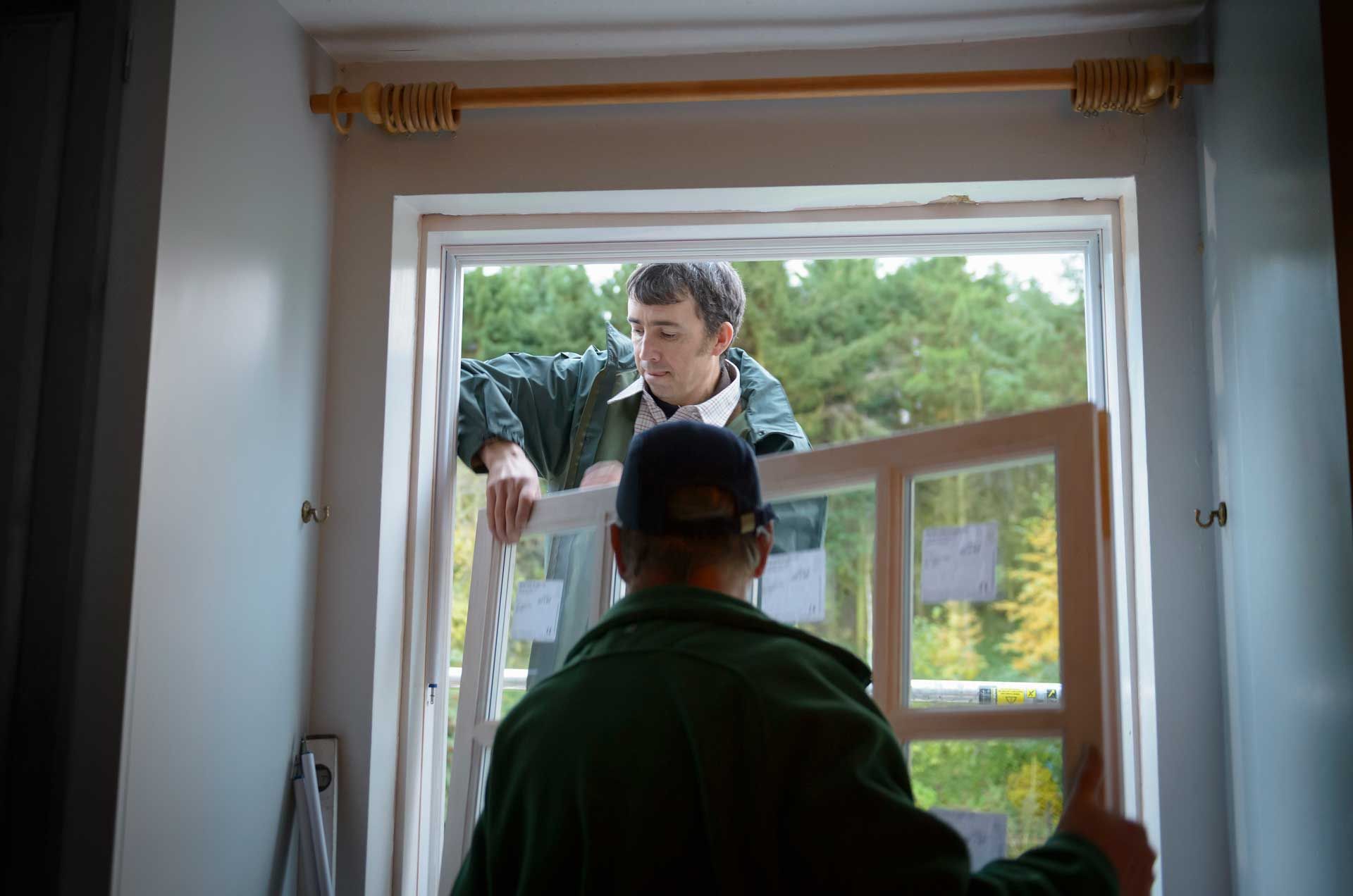 Two builders installing a new window in a house.