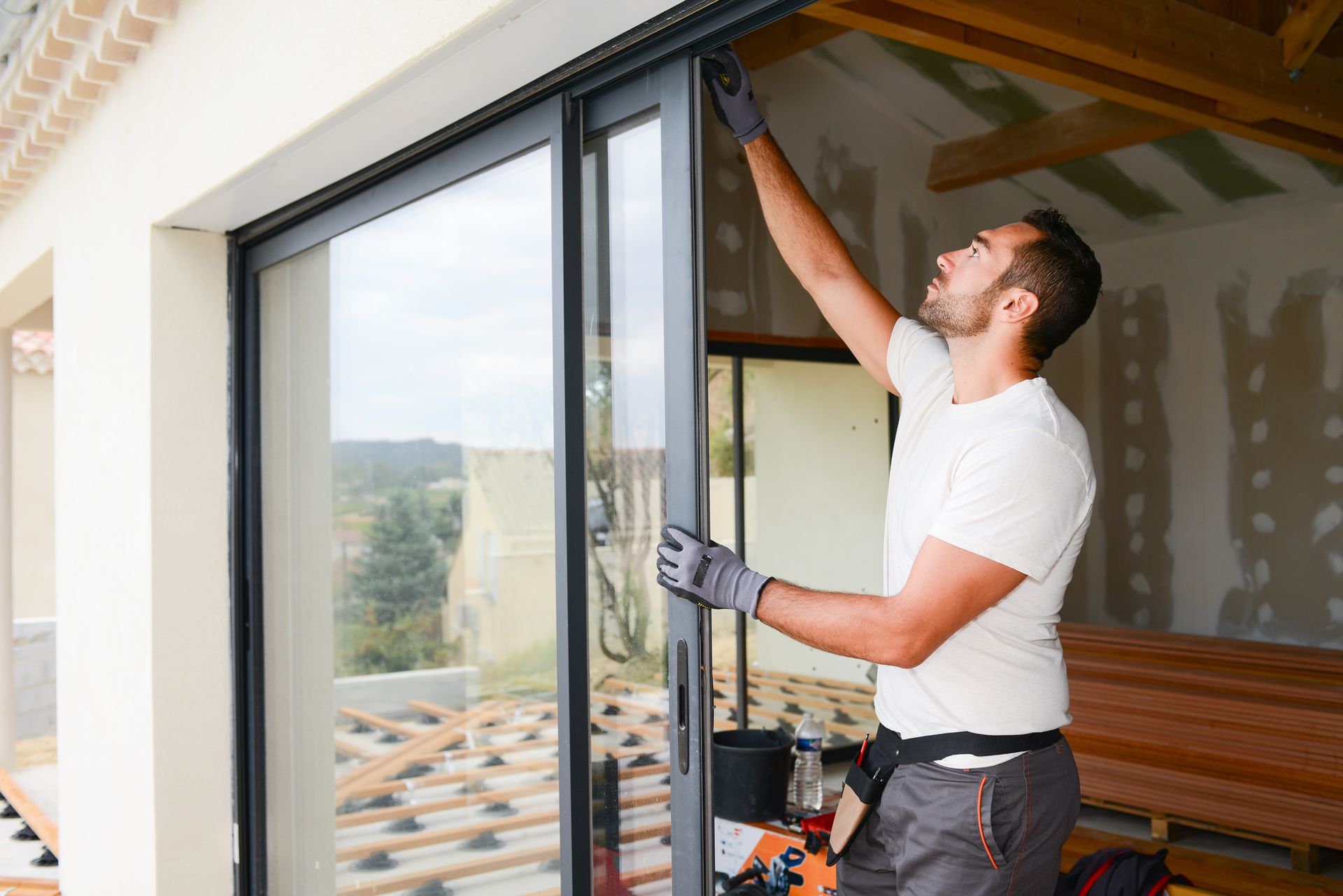 Window company worker installs black-framed sliding glass door in a modern home under construction. 