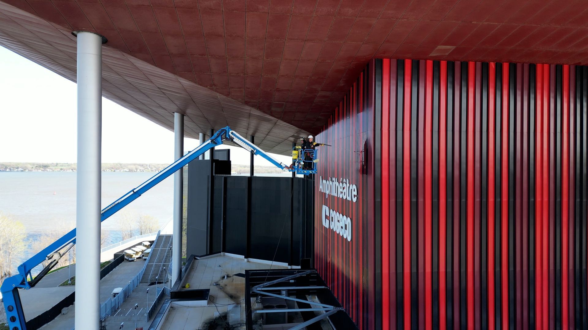 Un homme peint le mur rouge et noir d’un immeuble.