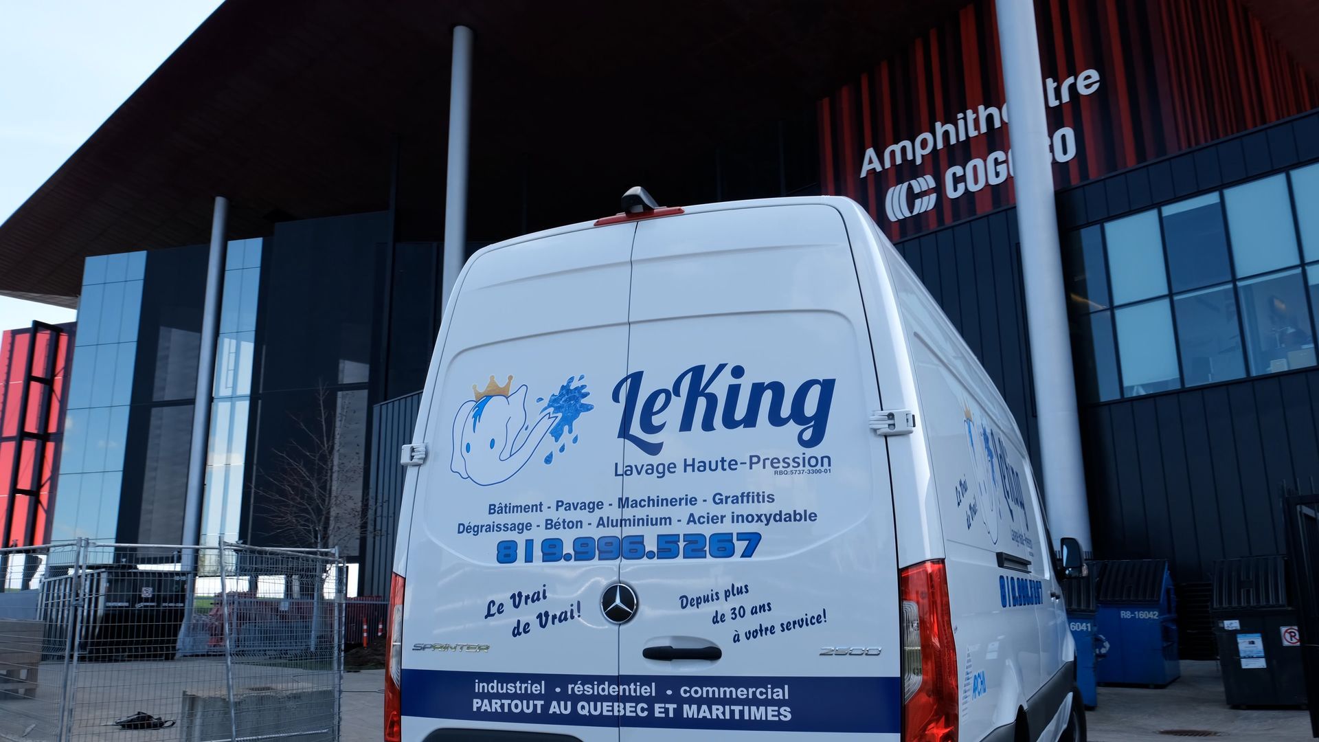 Une camionnette blanche avec le mot leking à l'arrière est garée devant un immeuble.