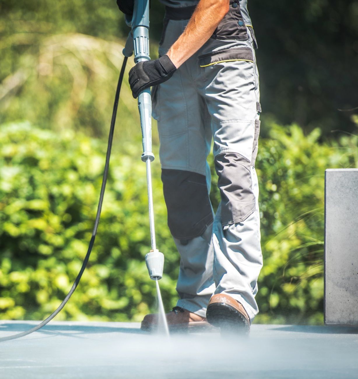 Un homme utilise un nettoyeur haute pression pour nettoyer une surface en béton.