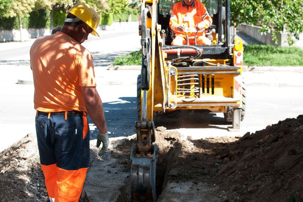Men Operating A Mini Digger In A Street — Excavator & Mini Excavator Hire in Boomerang Beach, NSW