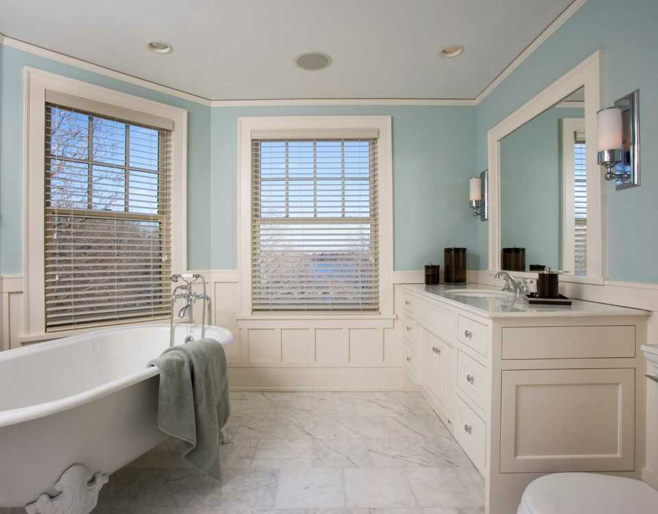 A bathroom with a tub , sink , mirror and window