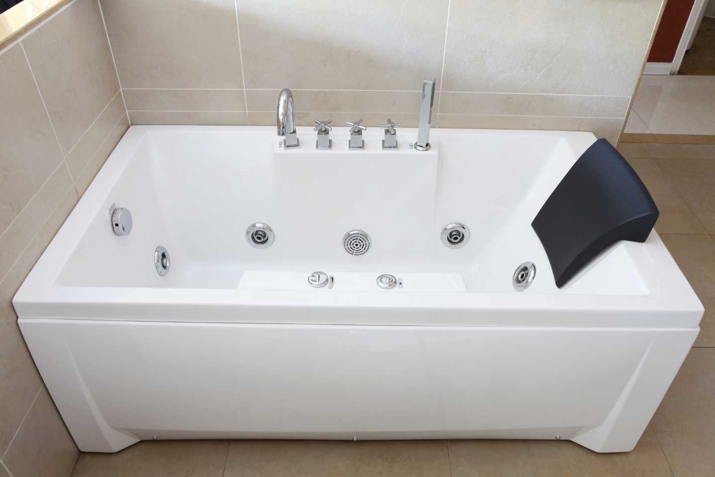 A white bathtub with a black pillow on the side