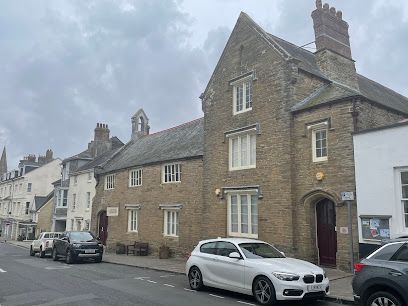 Stone building with arched doorway on a street with parked cars under an overcast sky.