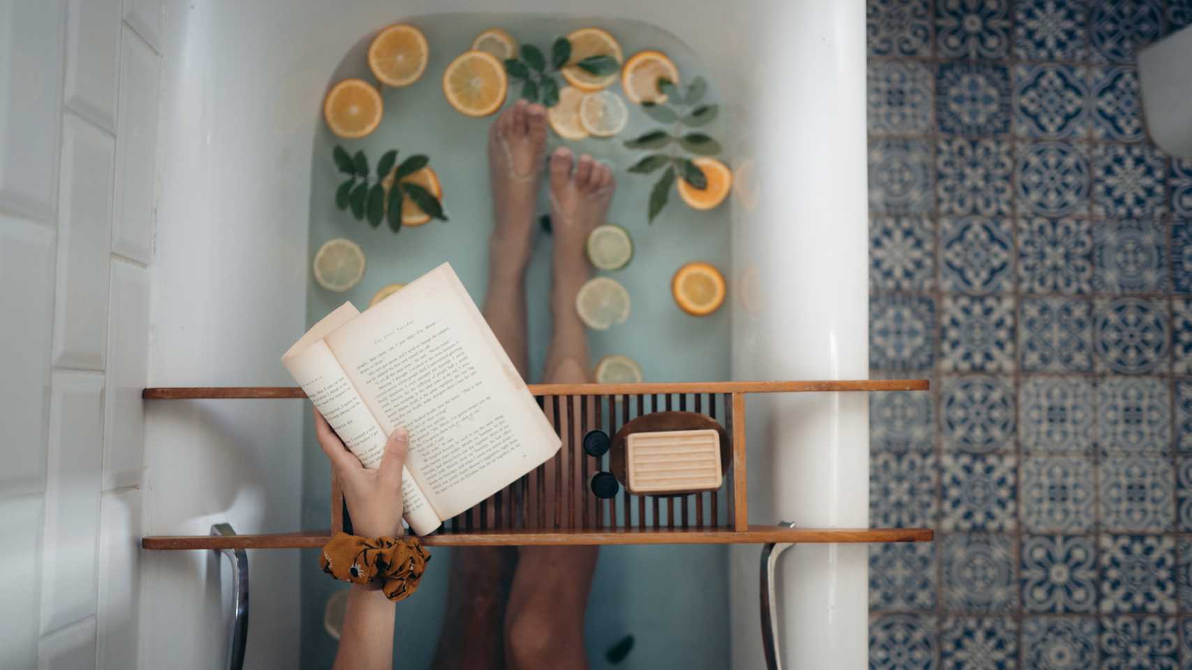 A woman is taking a bath with lemons and a book.
