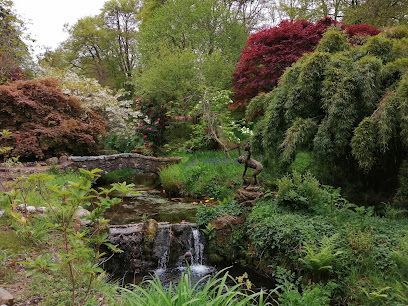 A lush garden scene with a small waterfall, stone bridge, and colorful trees.