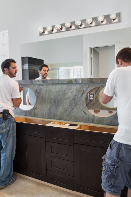 Two men are installing a large mirror in a bathroom.
