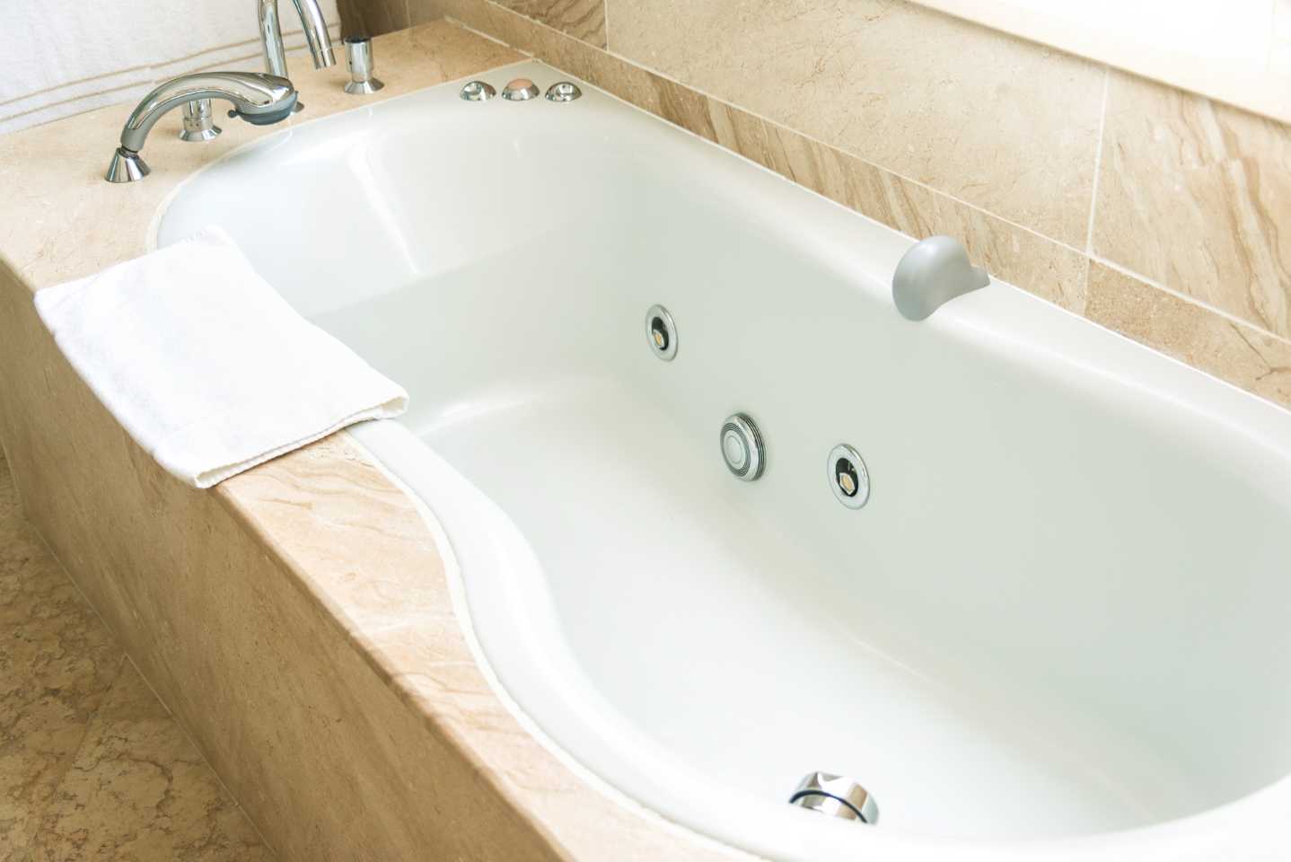 A white bathtub with a towel on the side of it in a bathroom.