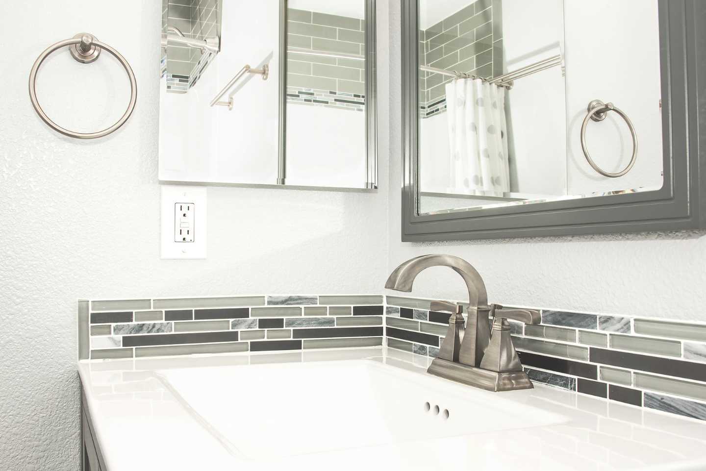 A bathroom with a sink , mirrors and towel rings.