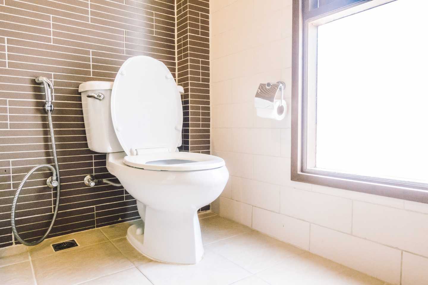 A toilet is sitting in a bathroom next to a window.