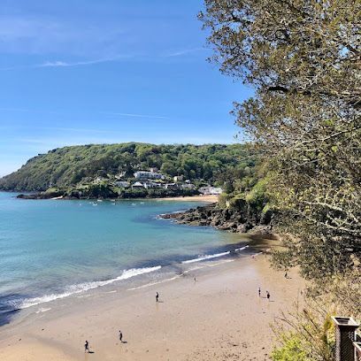 Beach scene with sandy shore, turquoise water, and green hillside under a blue sky.