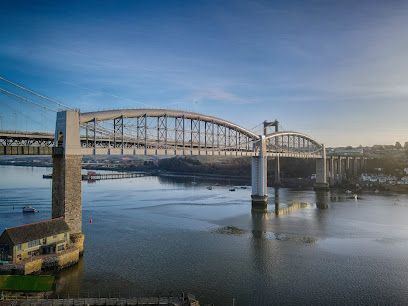 Arch bridge spanning a body of water under a clear blue sky. A building sits at the water's edge.