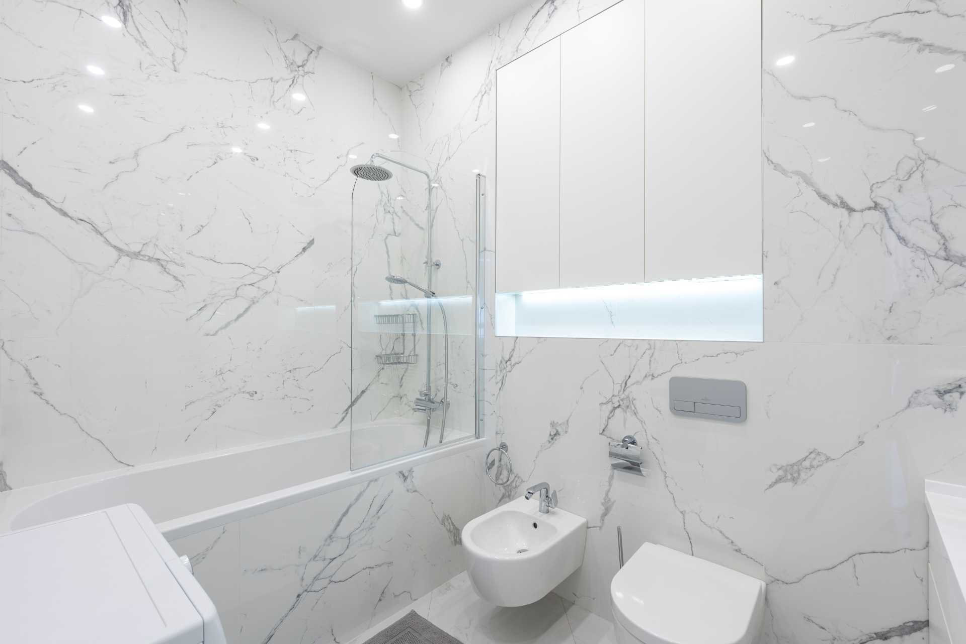A bathroom with white marble tiles , a toilet , a bidet and a bathtub.